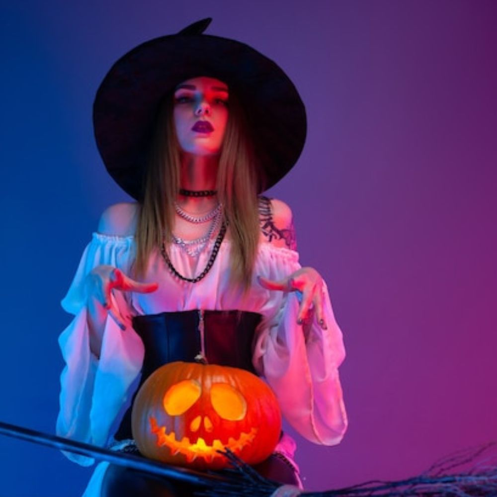 a-girl-in-a-witch-costume-for-halloween-with-a-broom-and-a-pumpkin-in-neon-light